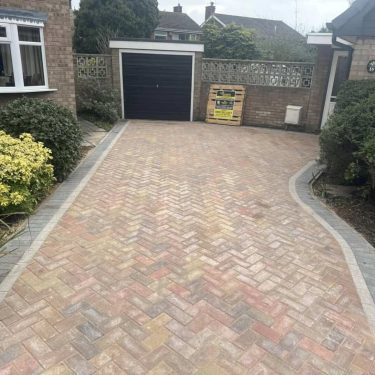 Herringbone block-paved driveway Warm-toned herringbone block paving installed across a residential driveway with a contrasting edge.