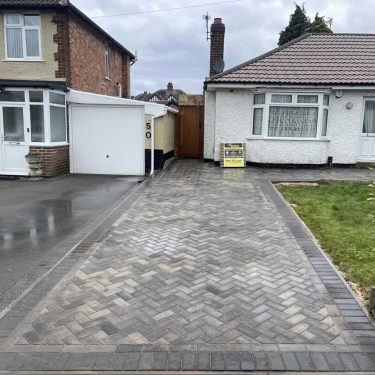 Grey herringbone block paving installed between a house frontage and a defined perimeter border.