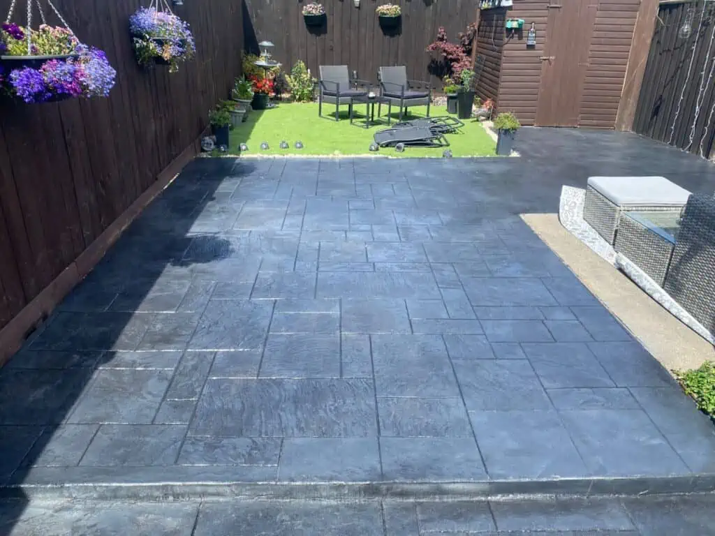 Gunmetal imprinted concrete patio Gunmetal imprinted concrete surface with a planned pattern beside a garden.