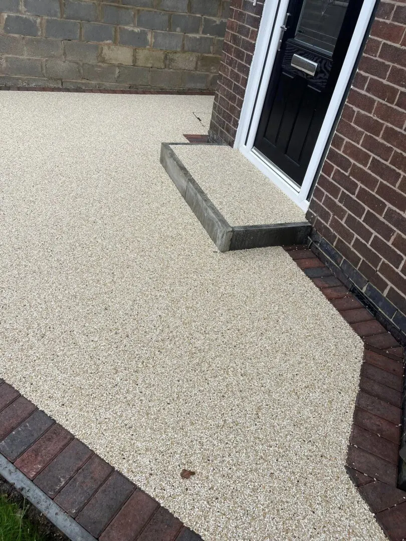 Resin-bound entrance surface meeting a paved edge beside a house.
