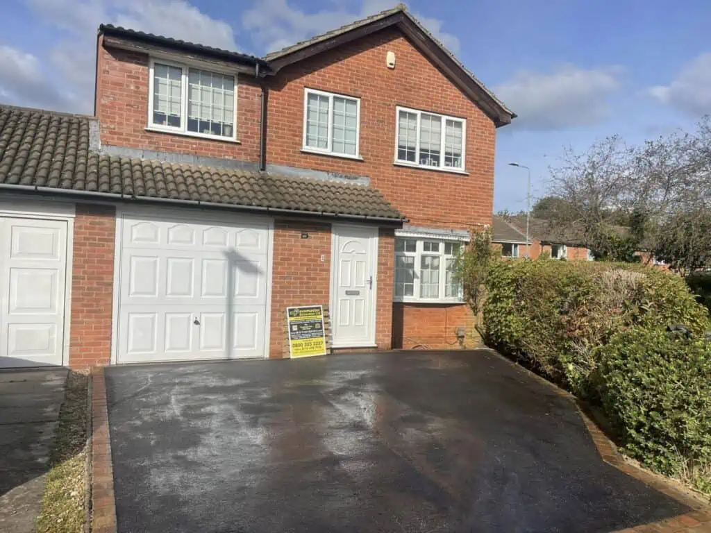 Smooth SMA tarmac finish Smooth dark SMA tarmac driveway beside a brick-built home and front garden.